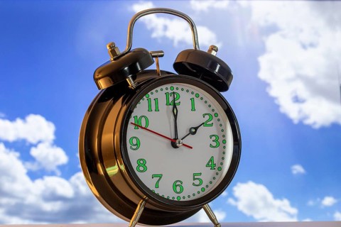 Symbolic image of the time change to summer time: close-up of an alarm clock in front of a blue sky