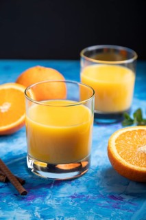 Glass of orange juice on a black and blue background. Hard light, contrast. Side view, close up