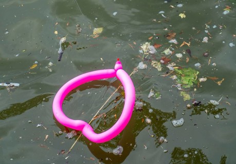 Pink balloon, shaped like a heart, floats in a dirty river