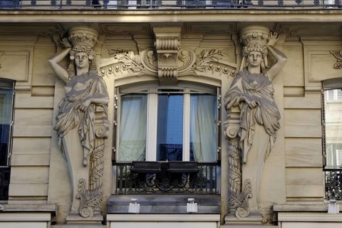 Two stone caryatids frame a window in the façade of a house in Paris as a decorative element.