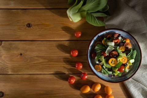 Vegetarian salad of pac choi cabbage, kiwi, tomatoes, kumquat, microgreen sprouts on a wooden