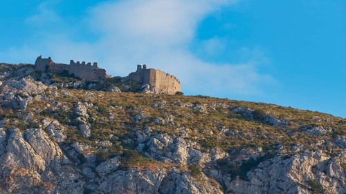 An ancient castle on the top of a rocky mountain under a blue sky with clouds, Archaic Castle,