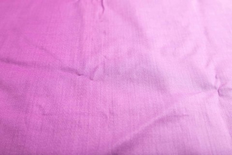 Fragment of smooth cotton purple tissue. Side view, natural textile background and texture