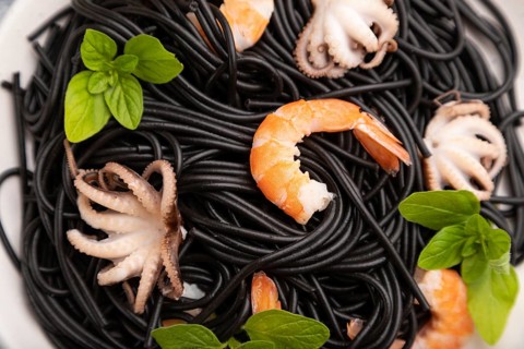 Black cuttlefish ink pasta with shrimps or prawns and small octopuses on gray wooden background and