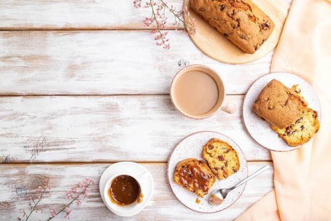 Homemade cake with raisins, almonds, soft caramel and a cup of coffee on a white wooden background