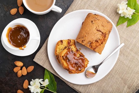 Homemade cake with raisins, almonds, soft caramel and a cup of coffee on a black concrete
