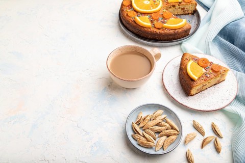 Orange cake with almonds and a cup of coffee on a white concrete background and blue linen textile.