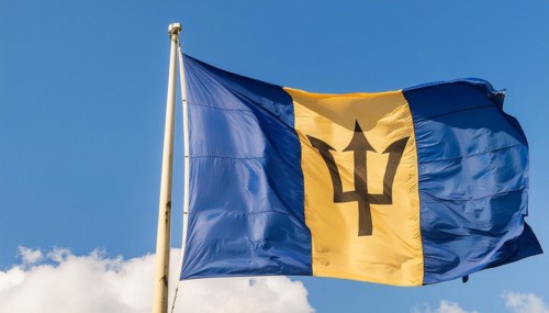 The Barbados flag flutters in the wind, isolated against a blue sky