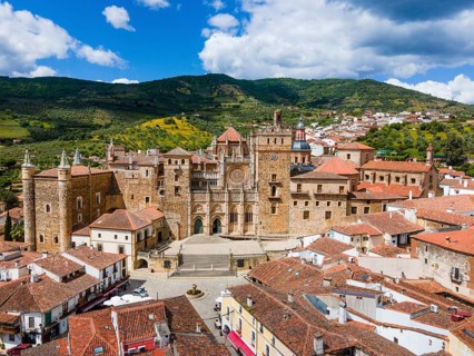 Aerial view of an old monastery with red roofs and surrounding hills under a blue sky in Spain. The