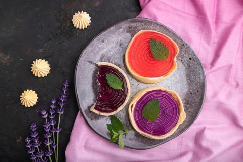 Sweet tartlets with jelly and milk cream with cup of coffee on a black concrete background and pink