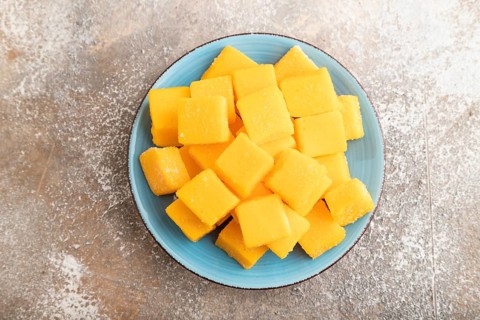 Dried and candied mango cubes on blue plate on brown concrete background. Top view, flat lay, close