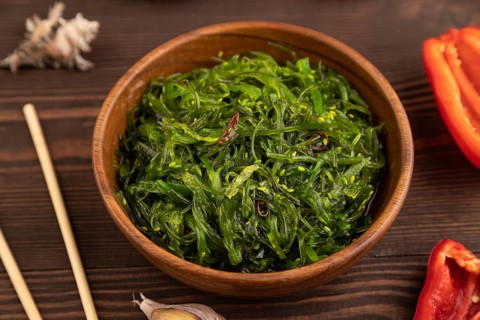 Chuka seaweed salad in wooden bowl on brown wooden background. Side view, close up, selective focus