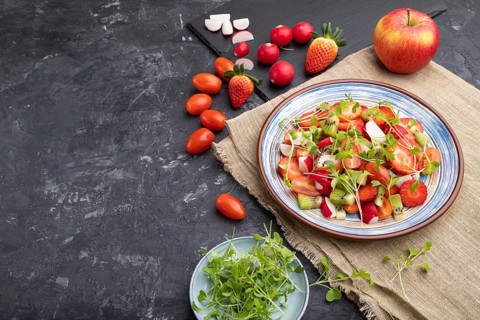 Vegetarian fruits and vegetables salad of strawberry, kiwi, tomatoes, microgreen sprouts on black