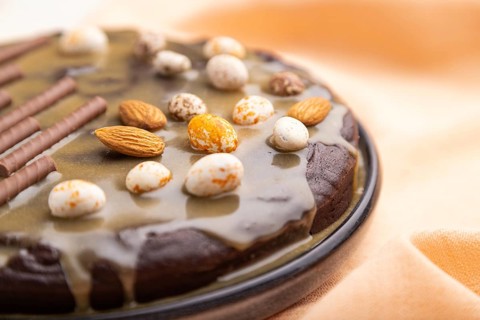 Homemade chocolate brownie cake with caramel cream and almonds with cup of coffee on a white