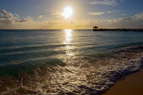 Sunset on the beach with a view of a jetty, breaking waves and shining sunbeams, Dominicus beach,