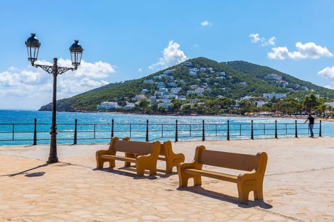Large square at the harbour of Santa Eularia des Rui with lantern and benches, behind the peninsula