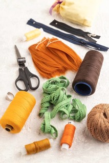 Sewing accessories: scissors, thread, thimbles, braid on gray concrete background. Side view, close