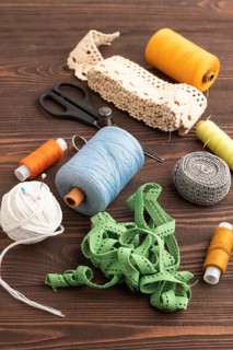 Sewing accessories: scissors, thread, thimbles, braid on brown wooden background. Side view, close