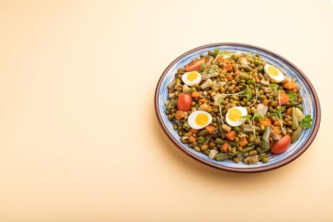 Mung bean porridge with quail eggs, tomatoes and microgreen sprouts on a pastel orange background.