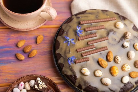 Homemade chocolate brownie cake with caramel cream and almonds with cup of coffee on a colored