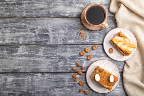 Honey cake with milk cream, caramel, almonds and a cup of coffee on a gray wooden background and