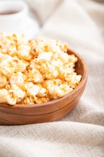 Popcorn with caramel in wooden bowl and a cup of coffee on a white wooden background and linen