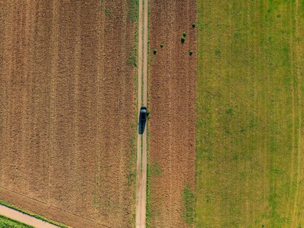 Aerial view of a car on a rural road between fields painted in green and brown colours, car