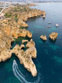 Rocks and cliffs rising out of the blue sea with a boat in the foreground, aerial view, Ponta da
