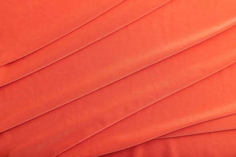 Fragment of red silk tissue. Top view, natural textile background and texture. wave concept,