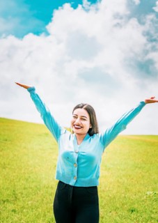 Happy young woman spreading arms in a beautiful field. Portrait of beautiful girl spreading arms