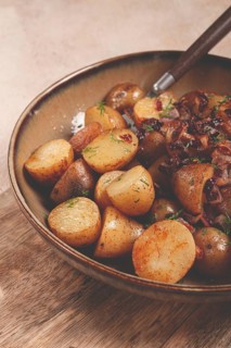 A bowl of perfectly roasted potatoes is served with caramelized onions and sprinkled with fresh