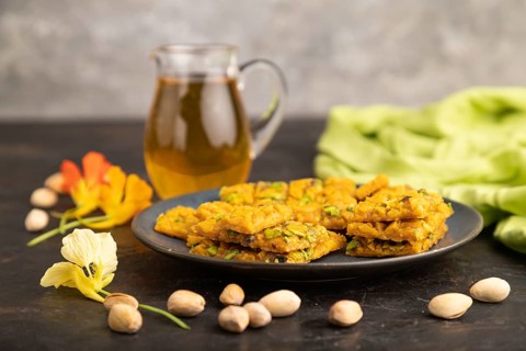 Traditional iranian dessert sohan with glass of green tea on a black concrete background and green