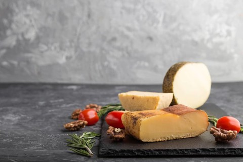 Smoked cheese and various types of cheese with rosemary and tomatoes on black slate board on a