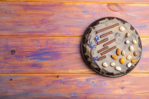 Homemade chocolate brownie cake with caramel cream and almonds on a colored wooden background. top