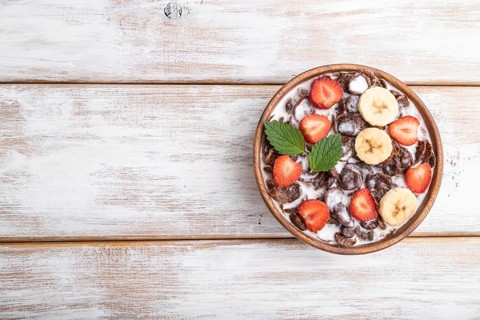 Chocolate cornflakes with milk and strawberry in wooden bowl on white wooden background. Top view,