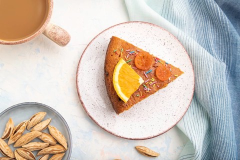 Orange cake with almonds and a cup of coffee on a white concrete background and blue linen textile.