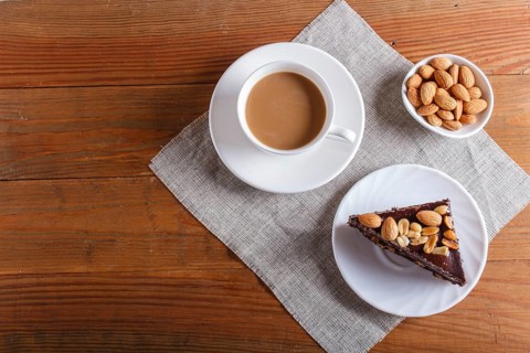 Chocolate cake with caramel, peanuts and almonds on a brown wooden background. cup of coffee, top