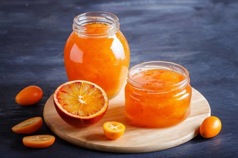 Orange and kumquat jam in a glass jar with fresh fruits on black wooden background. Homemade, close