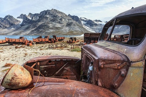 Rusted car and oil drums in front of steep mountains, remains of a US airbase from the Second World