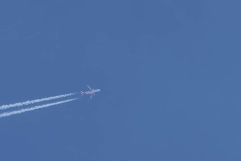 Airbus A320 aircraft of Easyjet airlines in flight with a contrail or vapour trail across a blue