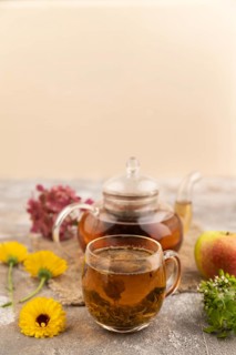 Red tea with herbs in glass teapot on brown concrete background and linen textile. Healthy drink