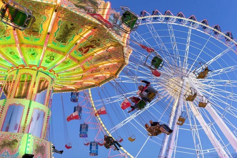 Illuminated chain carousel and Ferris wheel at night with cheerful people, funfair, wave flight,
