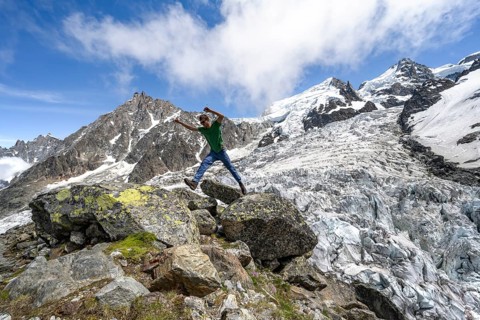 Mountaineer jumping from rock to rock, high alpine glaciated mountain landscape, La Jonction,