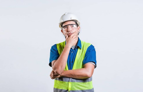 Young builder wondering looking up with hand on chin. Pensive builder man with hand on chin