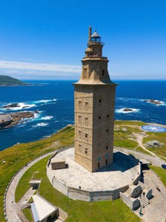 High lighthouse on the coast, rising proudly above the blue sea and the surrounding green areas,