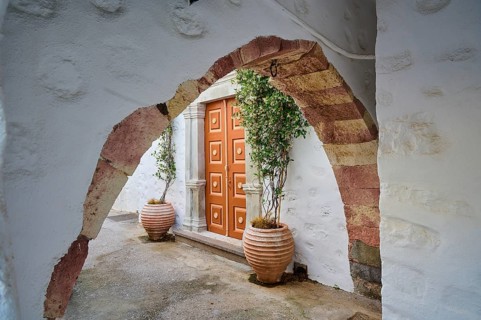 A historic stone Tor tor with plant pots and arches on a Greek island leading into a quiet