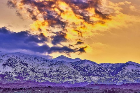 Dramatic sunset over snowy mountains with purple and orange sky and clouds, Lefka Ori, White