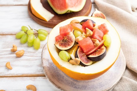 Vegetarian fruit salad of watermelon, grapes, figs, pear, orange, cashew on white wooden background