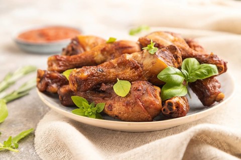 Smoked chicken legs with herbs and spices on a ceramic plate with linen textile on a brown concrete