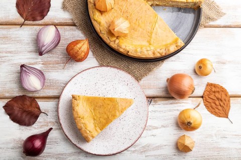Autumn onion pie decorated with leaves and cup of coffee on white wooden background and linen